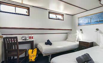 A cozy cabin with two single beds, a small desk with a chair, and a window. Cycling gear, including&hellip;