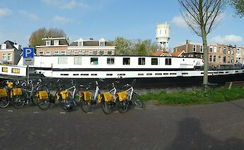 A white boat is moored along a canal with a row of bicycles parked in front. The backdrop includes&hellip;