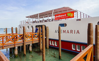 The Ave Maria boat docked at a wooden pier with people boarding.