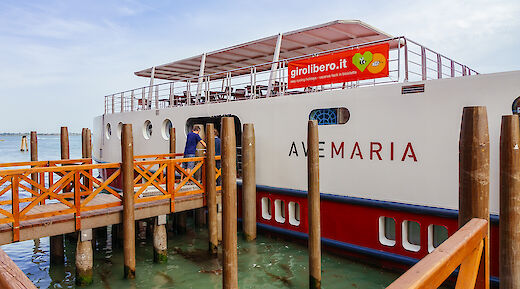 The Ave Maria boat docked at a wooden pier with people boarding.