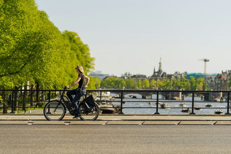 Lady cycling across a bridge in Amsterdam, Holland. Ugur Arpaci@Unsplash