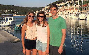 Three people posing by a waterfront in Croatia with sailboats and a town in the background under a&hellip;