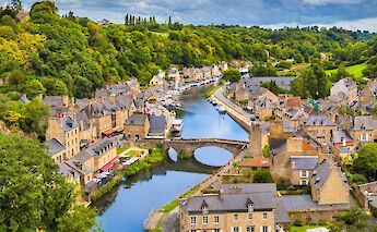 An aerial view of a village in France with stone buildings, a river with boats, and lush green&hellip;