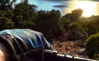 A gloved hand grips a bike handlebar, overlooking a coastal landscape with rocky shores, green…