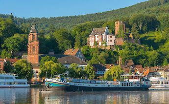 A boat named Allure docked in a town with historical architecture, including a church and a castle…
