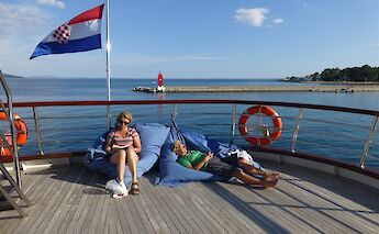 Two people relax with a book on bean bags on the sun deck of the Andela Lora, with a Croatian flag&hellip;