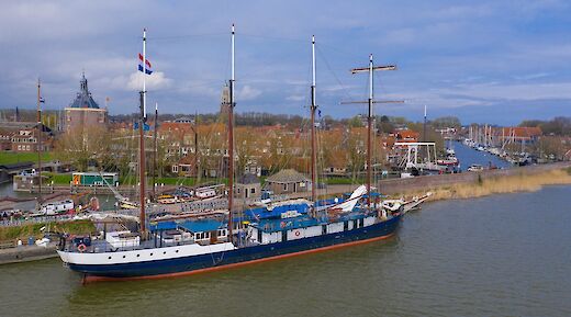 The Leafde fan Frysl&acirc;n is docked in a harbor with historic buildings and a tall church tower in the background.