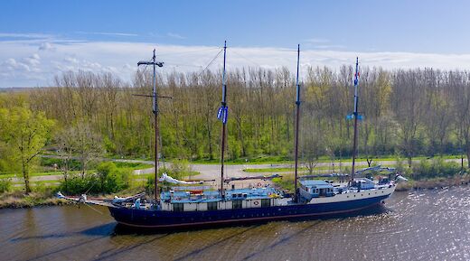 A large sailing vessel named Leafde fan Frysl&acirc;n is docked alongside a tree-lined canal under a bright blue sky.