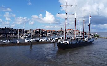 The Leafde fan Frysl&acirc;n sails near a harbor town with traditional houses, fluffy clouds, and a blue&hellip;