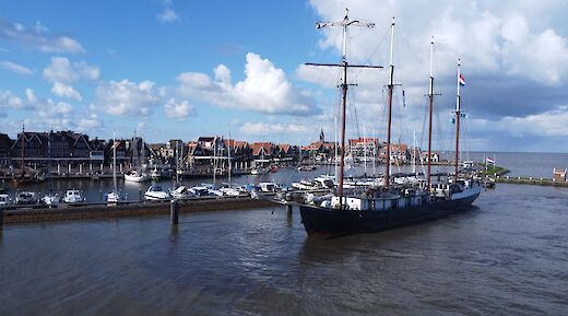 The Leafde fan Frysl&acirc;n sails near a harbor town with traditional houses, fluffy clouds, and a blue sky.