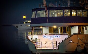 The stern of the "Princeza Diana" is illuminated at night with another vessel and a full…