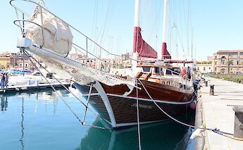 The bow and side view of the wooden sailing boat named Sundial docked in a marina.