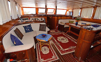 A cozy dining area on a boat with wooden furnishings, decorative rugs, couches, and tables.