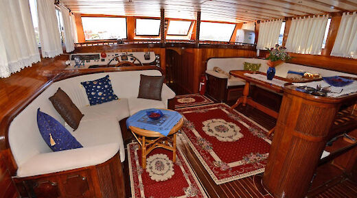 A cozy dining area on a boat with wooden furnishings, decorative rugs, couches, and tables.