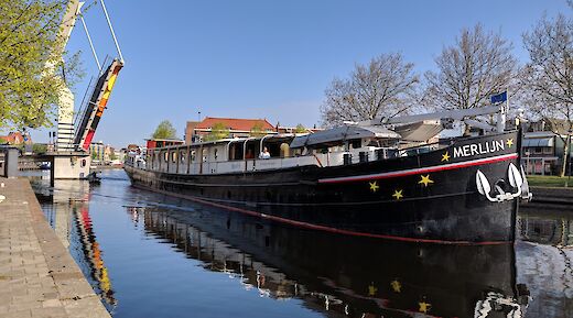 Merlijn boat is seen in a canal near Haarlem with a raised drawbridge in the background on a clear day.