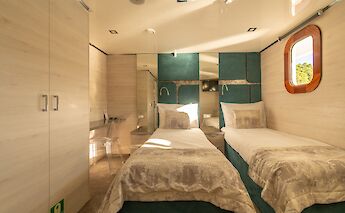 A cozy twin cabin on a boat with modern furnishings, featuring two single beds, a window with a…