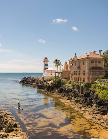 A picturesque coastal view in Cascais, Portugal, featuring a lighthouse and elegant houses by the water's edge.