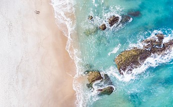 Aerial view of waves crashing on rocks along a sandy beach in Cascais, Portugal.