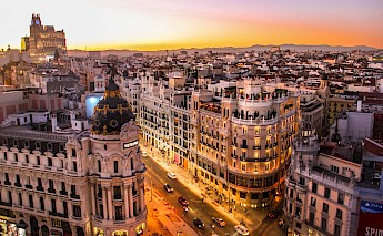 Calle Gran Vía in Madrid, Spain, at sunset, showing the iconic Metrópolis building and surrounding architecture.