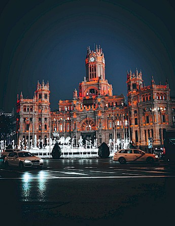The Palacio de Cibeles in Madrid, Spain, illuminated at night with cars passing in front.