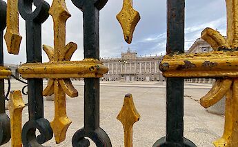 An ornate iron gate with gold accents frames a view of a large neoclassical building in Madrid, Spain.