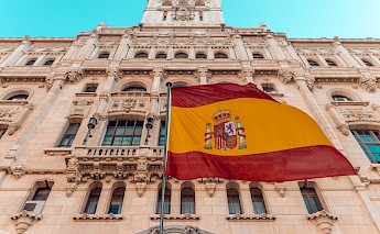 The Spanish flag waving in front of an ornately carved stone building in Madrid, Spain.