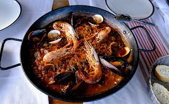 A pan of seafood paella with shrimp, clams, and mussels on a table with white linens.