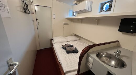 A cabin interior on the Clair de Lune boat, showing a bed with folded towels, a sink, coat hooks, and small porthole windows.