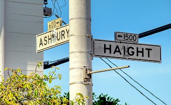 Street signs for Haight and Ashbury streets on a post, surrounded by green foliage against a blue sky.