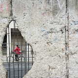 Woman cycling through hole in Berlin Wall. Unsplash:Morgana Bartolomei