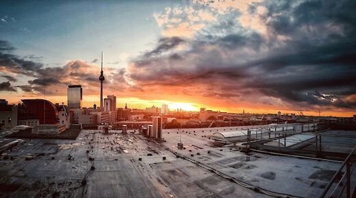 A view of Berlin at sunset, featuring city buildings with the TV Tower prominently visible under a dramatic sky.
