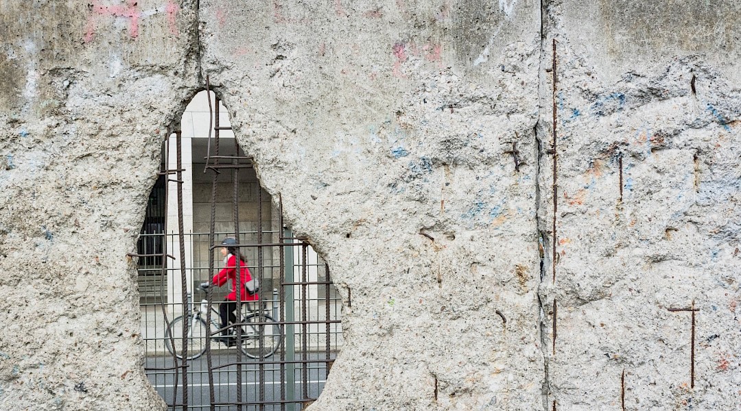Woman cycling through hole in Berlin wall. Unsplash:Morgana Bartolomei