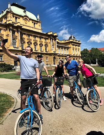 A group of cyclists taking a selfie in front of the Croatian National Theatre in Zagreb.