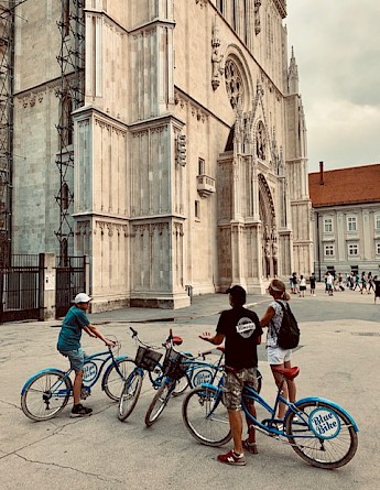 Cyclists stopped near a cathedral in Zagreb, admiring the architecture.