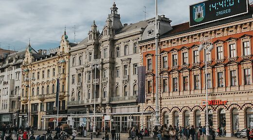 A view of Ban Jelačić Square in Zagreb, Croatia, with historic buildings lining the bustling square. People are visible walking and gathering in the area.
