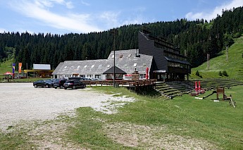 A lodge-style building in a mountainous area of Mount Trebevic, with parked cars and a forested backdrop.