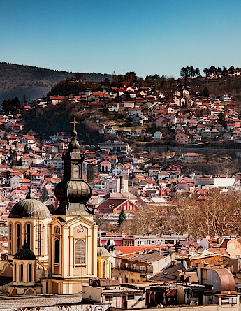 A view of a hillside neighborhood in Sarajevo with densely packed houses and a church in the foreground.