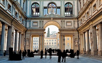 View of the Uffizi Gallery courtyard in Florence, Italy, featuring an ornate archway and people silhouetted against the architecture.