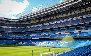 The Santiago Bernabéu Stadium in Madrid, showing rows of empty blue seats and the pitch.