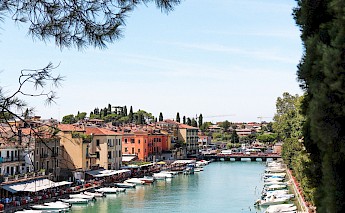 Colorful buildings and restaurants line the banks of the river Adige in Verona, with small boats docked alongside.