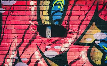 A vibrant graffiti mural on a brick wall features abstract shapes and a bright color palette, with a spray paint can placed in a recess.