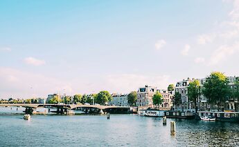 A bridge over a waterway with historic buildings and trees lining the canal in Amsterdam, Holland.