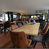 A spacious dining area with wooden tables, assorted chairs, and vases with flowers, providing a bright and welcoming atmosphere.