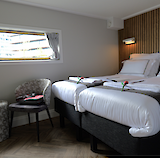 A well-appointed cabin with two neatly made twin beds, a small window, and cozy seating, showcasing a simple yet elegant decor.