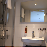 A modern bathroom featuring a shower, sink, and large mirror, with white tiles and a simple, clean design.
