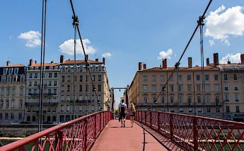 French couple holding hands while crossing Lyon's Saint-Vincent bridge. Laurine Peyrard@Unsplash
