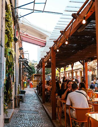 People dining at an outdoor space in Lisbon, surrounded by greenery and urban architecture.