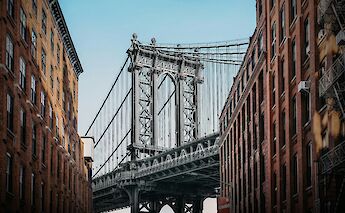 A view of the Manhattan Bridge framed by red brick buildings in Brooklyn, New York.