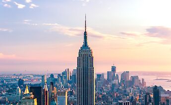 The Empire State Building stands prominently against a colorful sky during sunset, with the New York City skyline in the background.