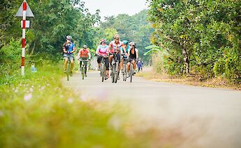 Cyclists riding along a rural road surrounded by greenery in Vietnam.